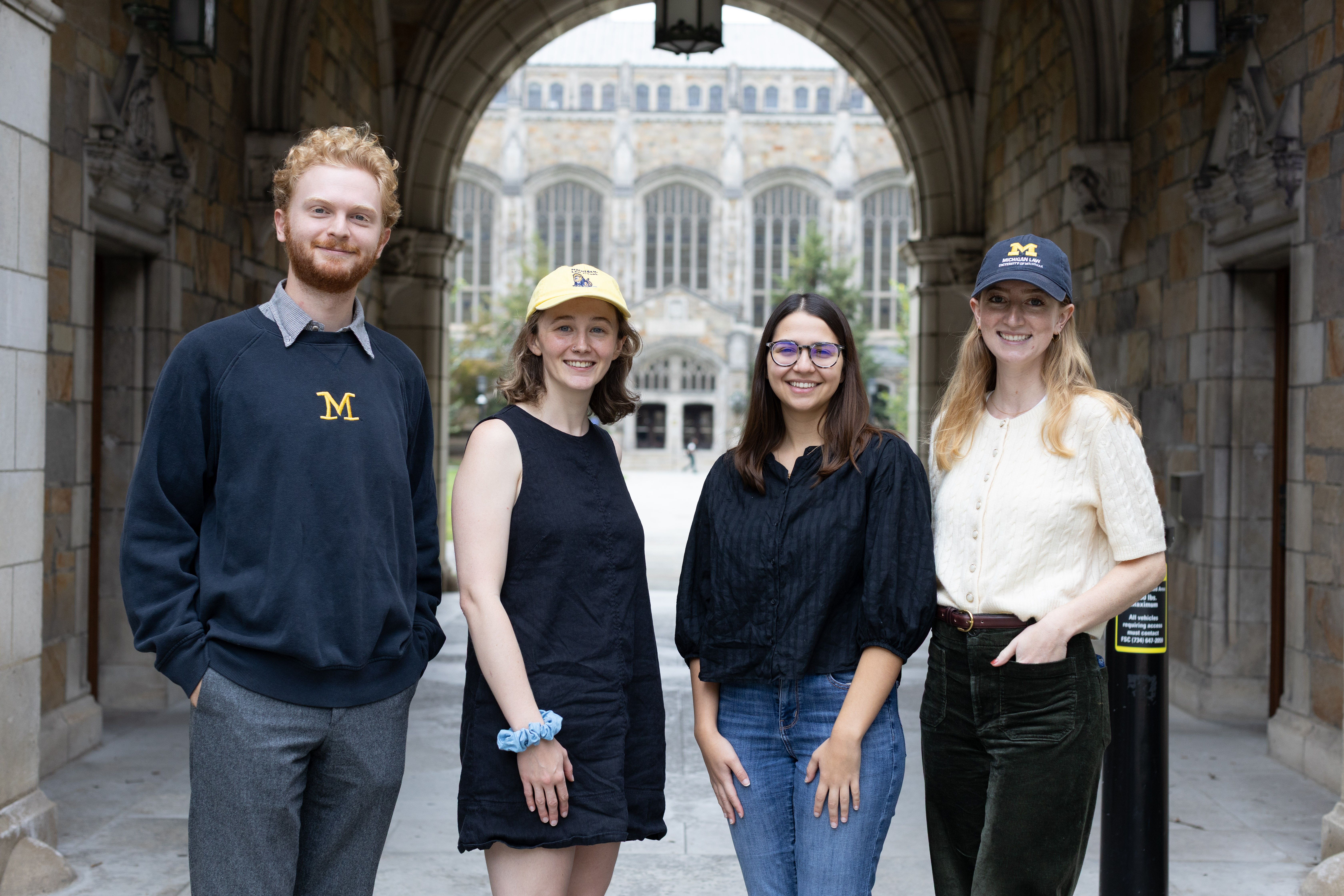 Four law students stand in front of the M5ichigan law quad; they have UMichigan branded hats and sweaters.