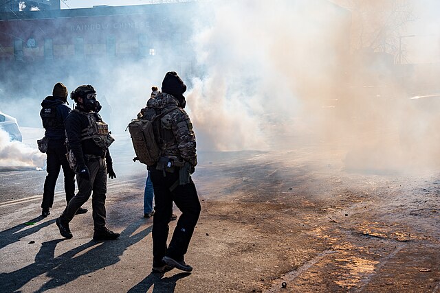 Federal agents in Minneapolis stand in front of a cloud of tear gas smoke.