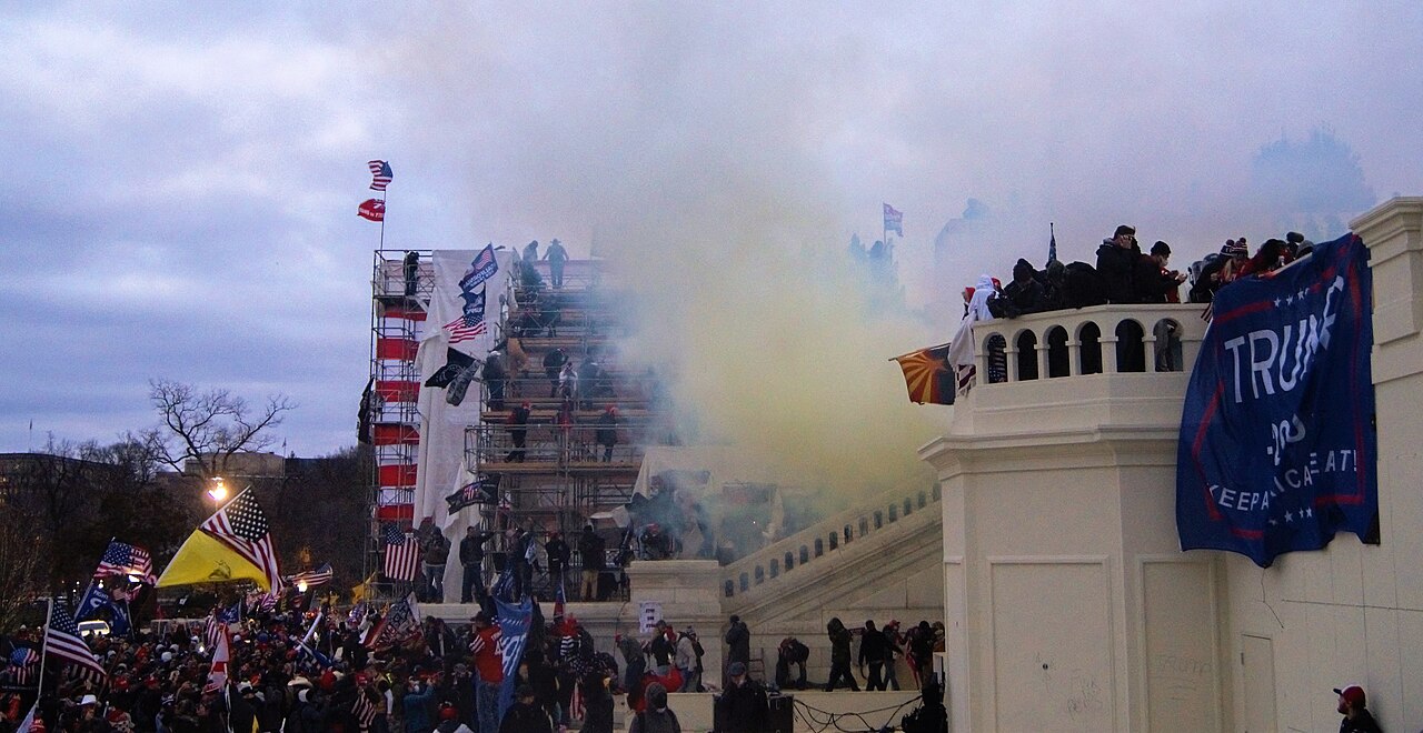 Protesters outside the United States Capitol on January 6, 2021 with flags. Tear gas used to dispurse the crowd is visible.